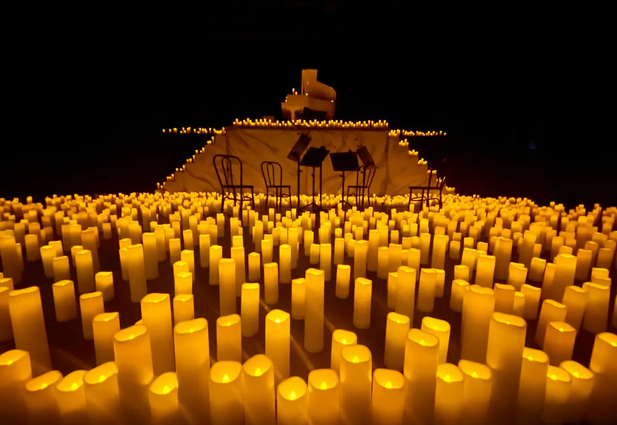 A dark stage covered in glowing candles, with a grand piano and chairs at the back