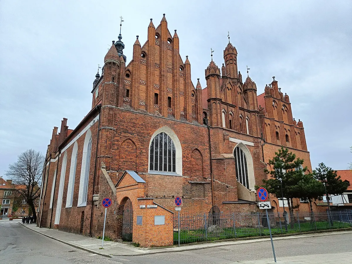 The red brick east end of St Catherine's Church in Gdańsk under a pale sky, with stepped gables, pinnacles and a copper-topped tower behind