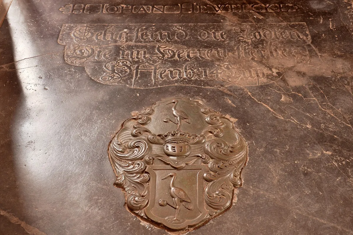 The dark stone tombstone of Johannes Hevelius in St Catherine's Church, with carved lettering and a coat of arms showing two storks