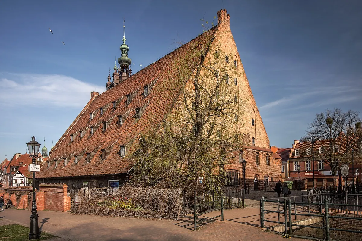 The Great Mill in Gdańsk on a spring day, a very steep tiled roof with rows of dormers and the green spire of St Catherine's behind it